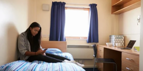Image of an expat student sat on her bed in her university accommodation room